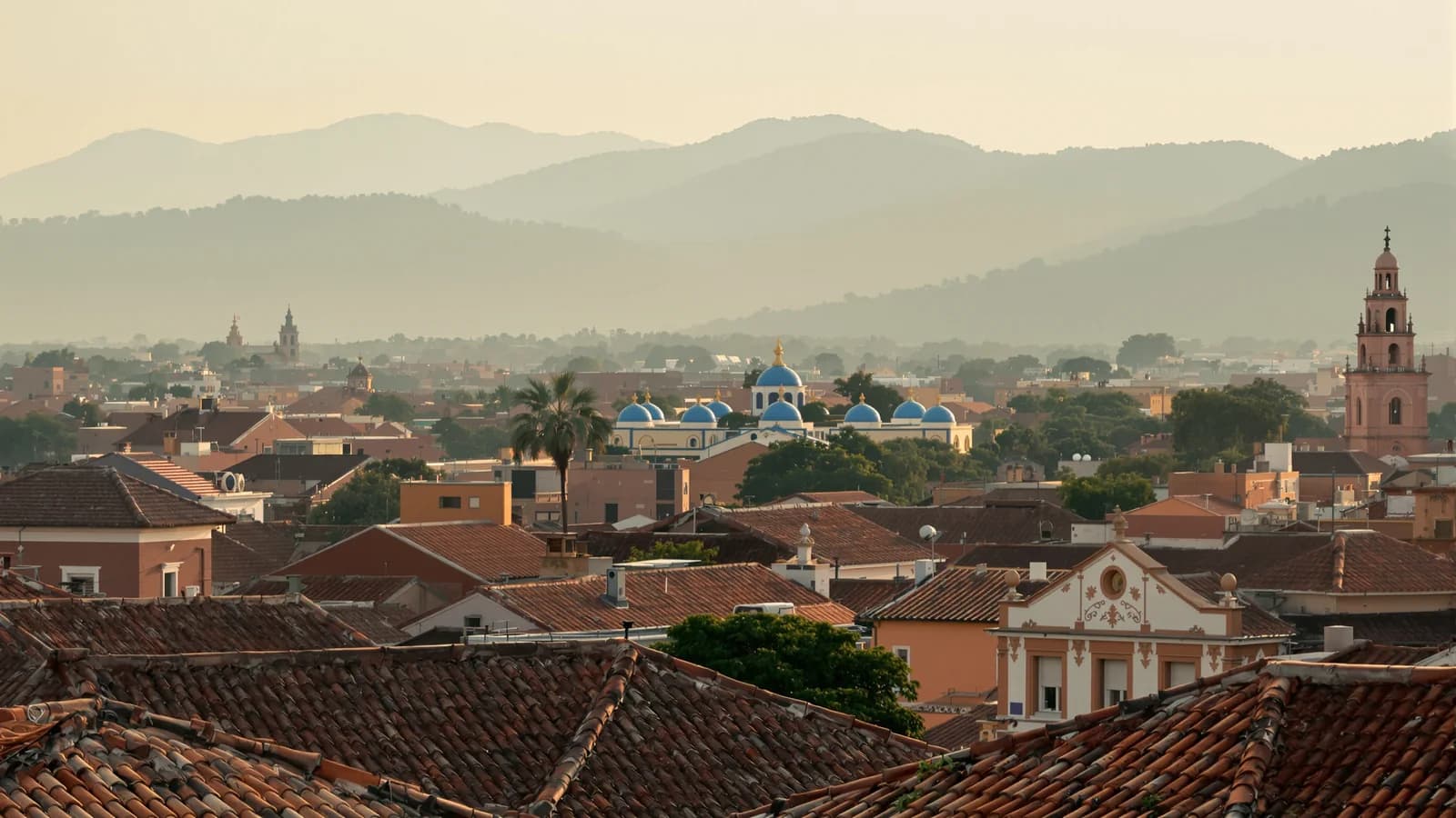 Blick über die Dächer von Cuenca im Abendlicht, blaue Kirchenkuppeln in der Bildtiefe, grüne Hügel dahinter.