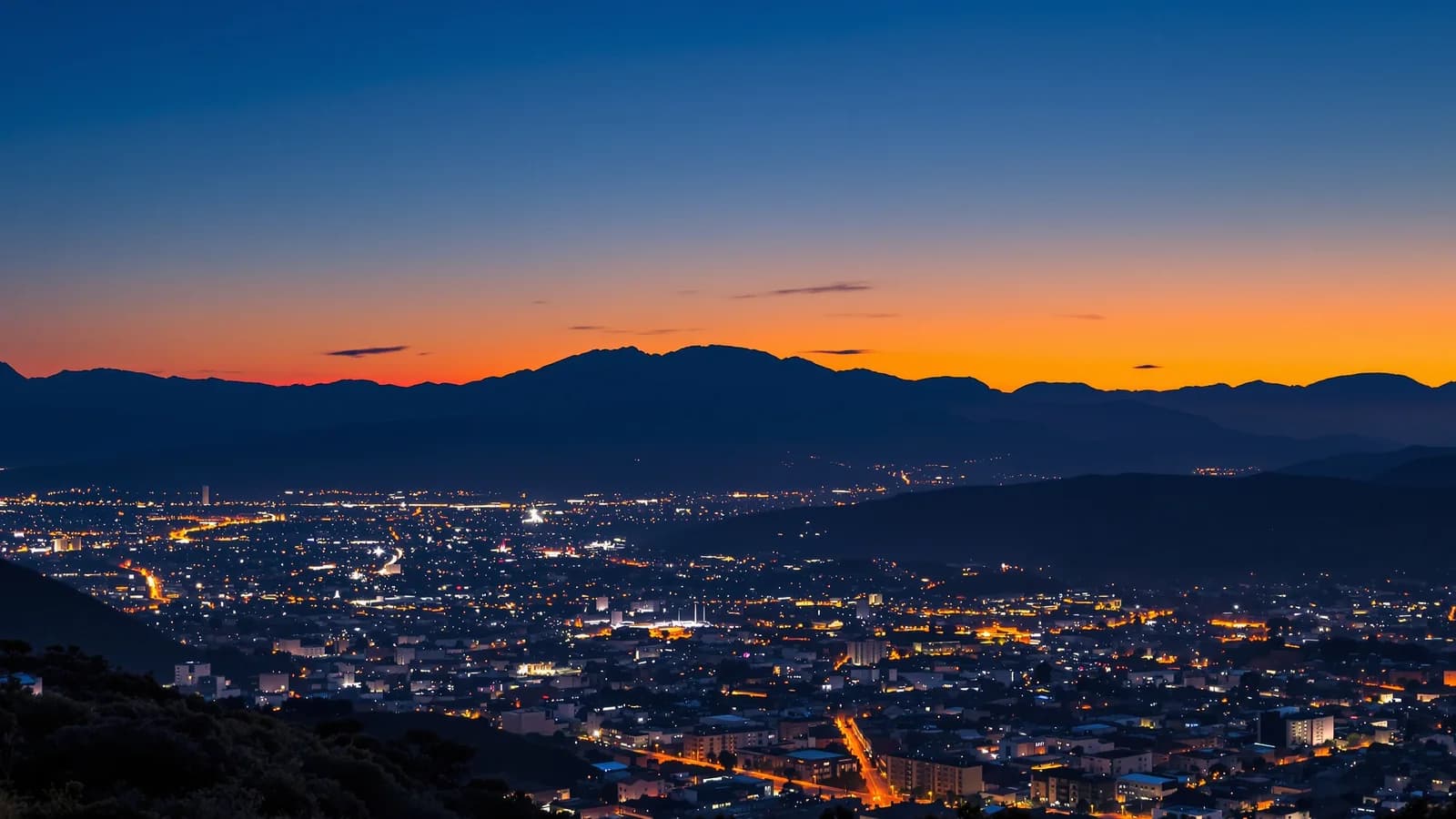 Lichtermeer einer Andenhauptstadt in der Abenddämmerung, dunkle Bergsilhouetten ringsum.