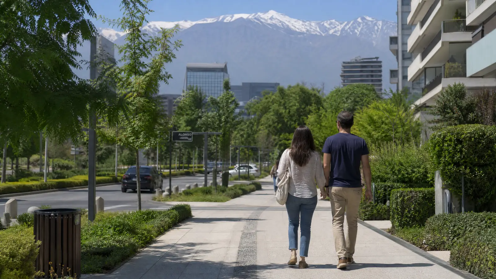 Paar geht entspannt durch ein gepflegtes Viertel in Santiago mit modernen Gebaeuden und den Anden im Hintergrund.