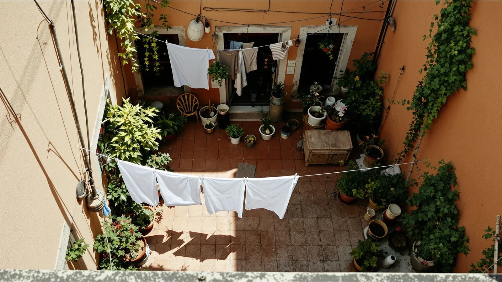 Blick von oben in einen bewohnten Innenhof mit Wäscheleine, Topfpflanzen und abgetretenem Fliesenboden.