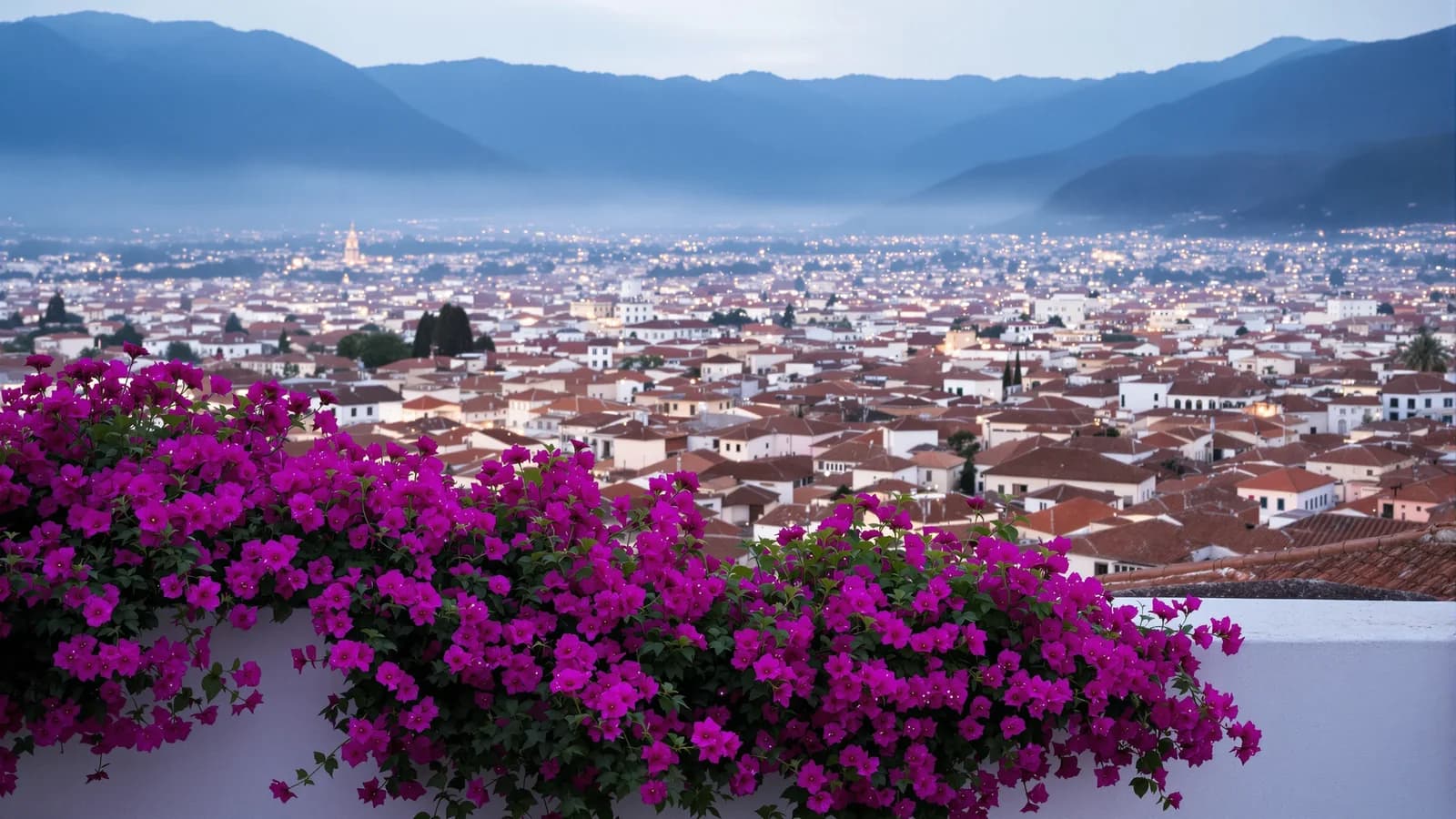 Blick von einer Dachterrasse mit blühender Bougainvillea über die Terrakotta-Dächer einer Andenstadt in der Abenddämmerung, Lichter gehen an, Berge im Dunst.